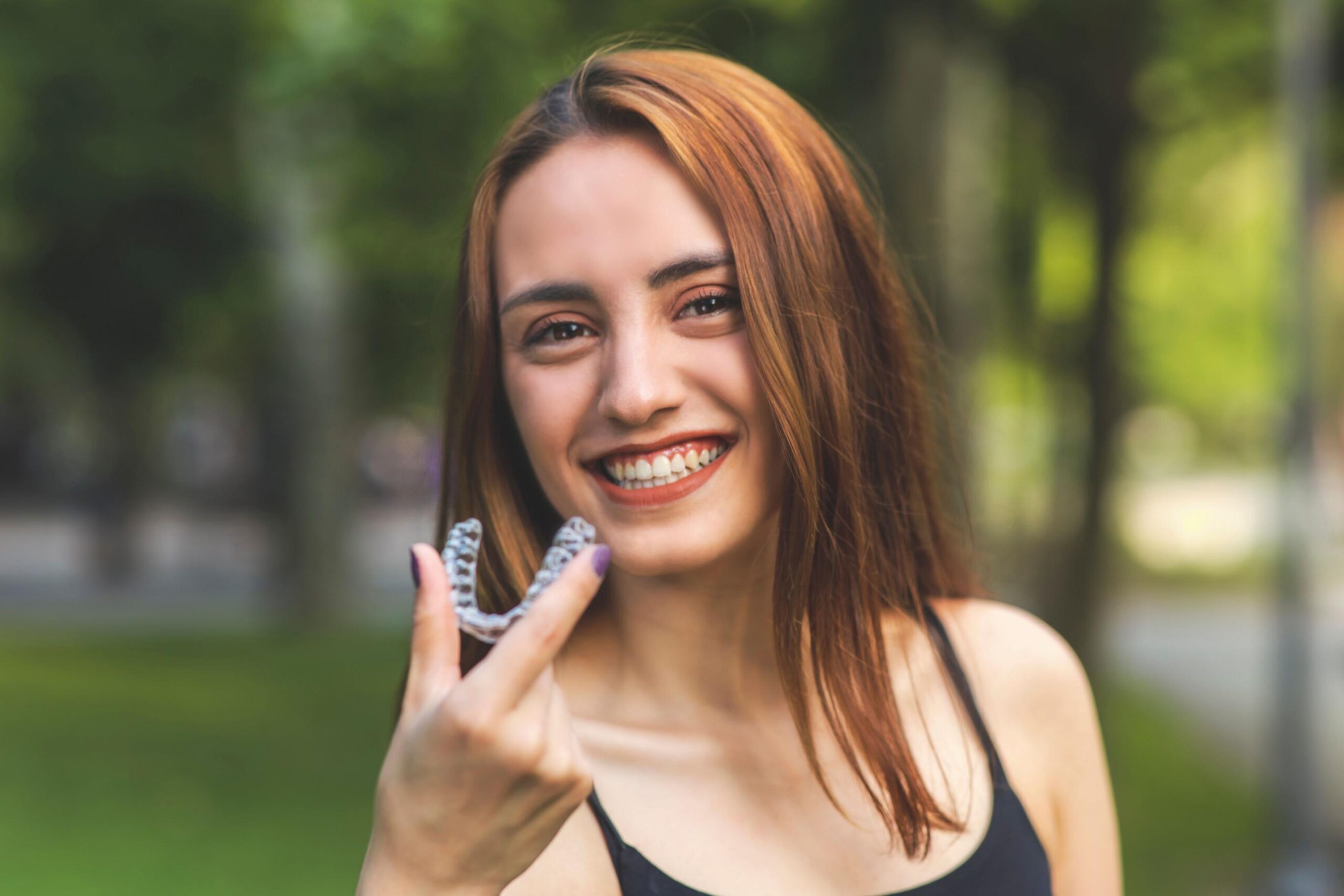 Smiling patient holding clear aligners outdoors