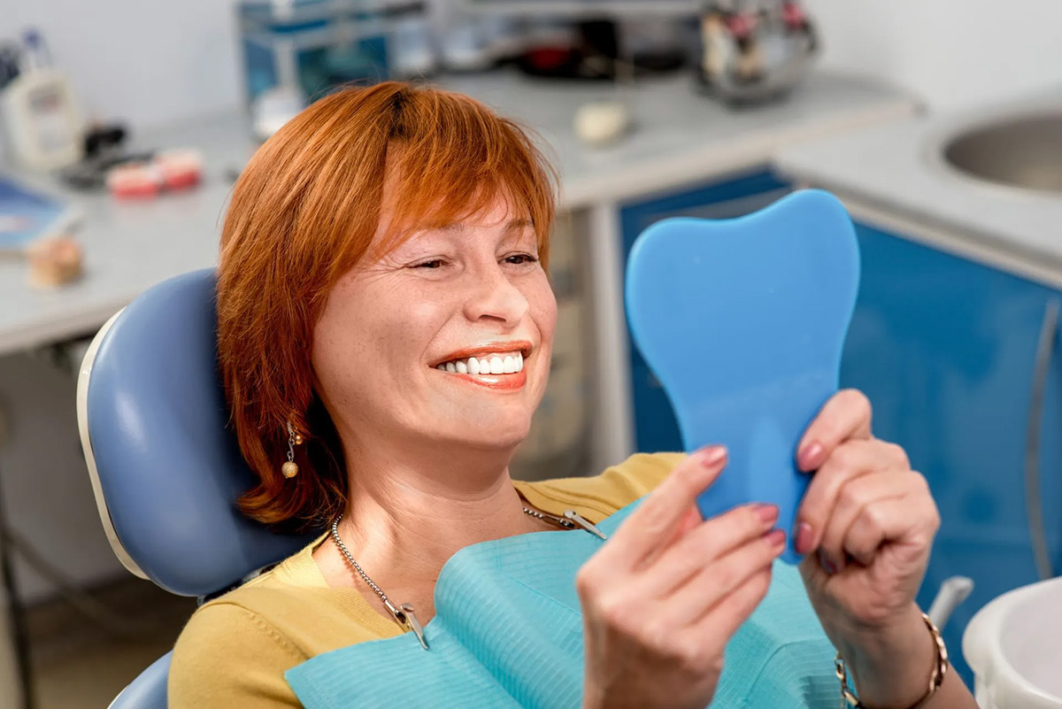 Dental patient smiling while viewing results in a hand mirror